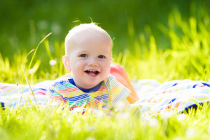 Adorable baby boy eating apple playing on colorful blanket in green grass. Child having fun on family picnic in summer garden. Kids eat fruit. Healthy nutrition for little child. Kid with apples.